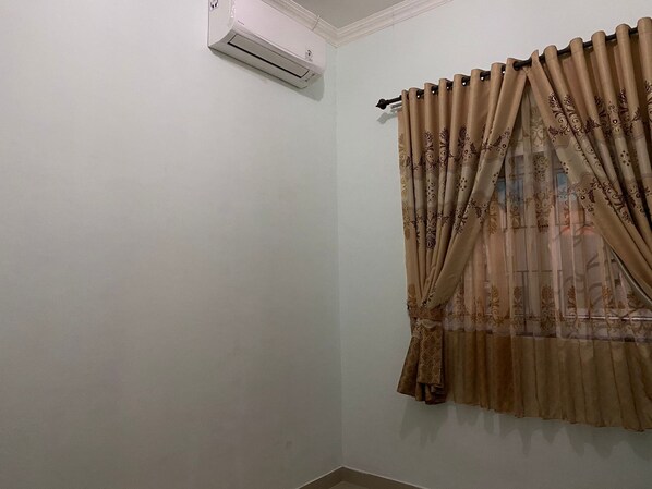 A room with a white wall, a beige curtain with a floral pattern, and a ceiling-mounted air conditioning unit.