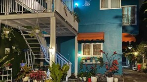 Un immeuble de deux étages doté d’un balcon, de plantes en pot et d’un escalier.
