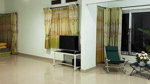 Un salon spacieux avec un téléviseur à écran plat posé sur un meuble blanc, un fauteuil vert et un balcon agrémenté d’une plante en pot.