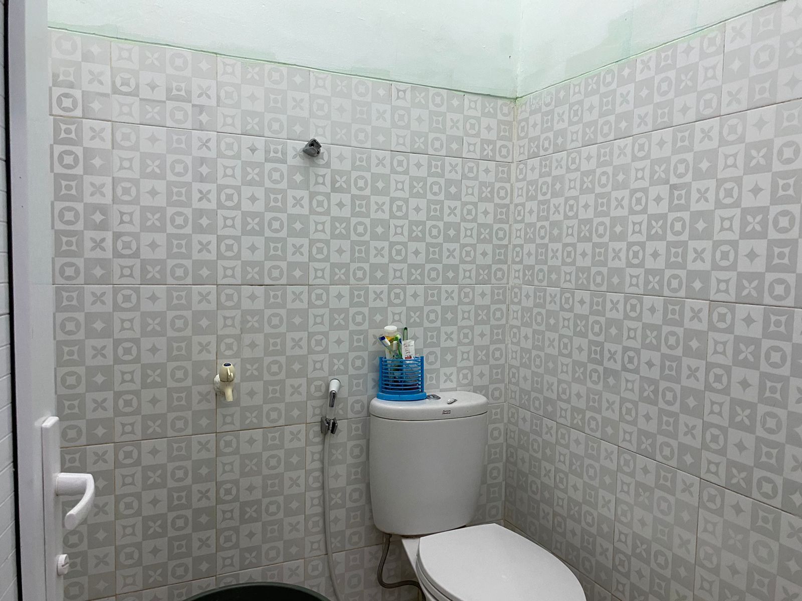 A small, enclosed bathroom with a toilet, a hand dryer, and a blue bottle holder on the wall.