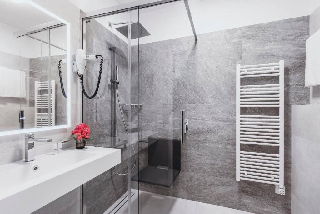A modern bathroom with a glass-enclosed shower, a white sink, and a towel rack.