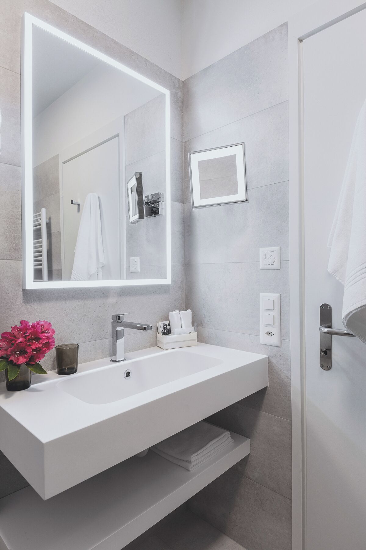 A modern bathroom with a large mirror, white sink, and a towel rack.