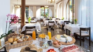 A breakfast buffet with various foods, including pastries, fruits, cheeses, and meats, set up in a well-lit dining area with tables and chairs. - Garni Elena (Losone)