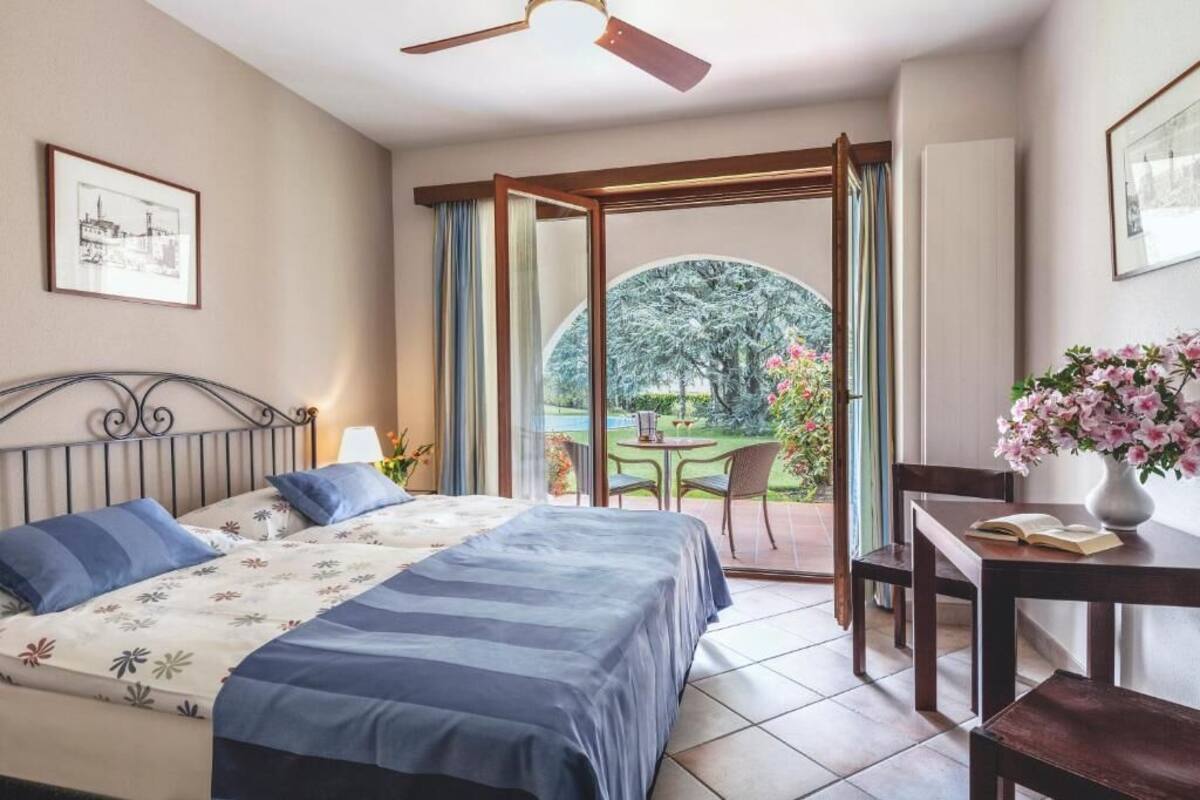 A bedroom with a bed, a desk, and a view of a garden through a glass door.