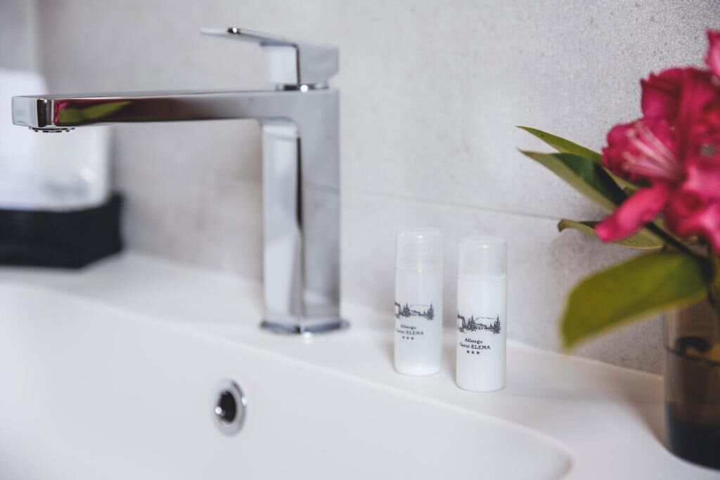 A bathroom sink with a chrome faucet and two bottles of 'Allergy New ELENA' on the counter.