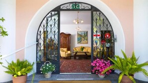 A hotel entrance with a wrought iron gate, a sofa, a table, and potted plants. - Garni Elena (Losone)