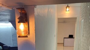 Ein schmaler Flur mit künstlichem grünen Teppich, einer weißen Wand und einer Tür zu einem Raum mit Schreibtisch und Laptop.