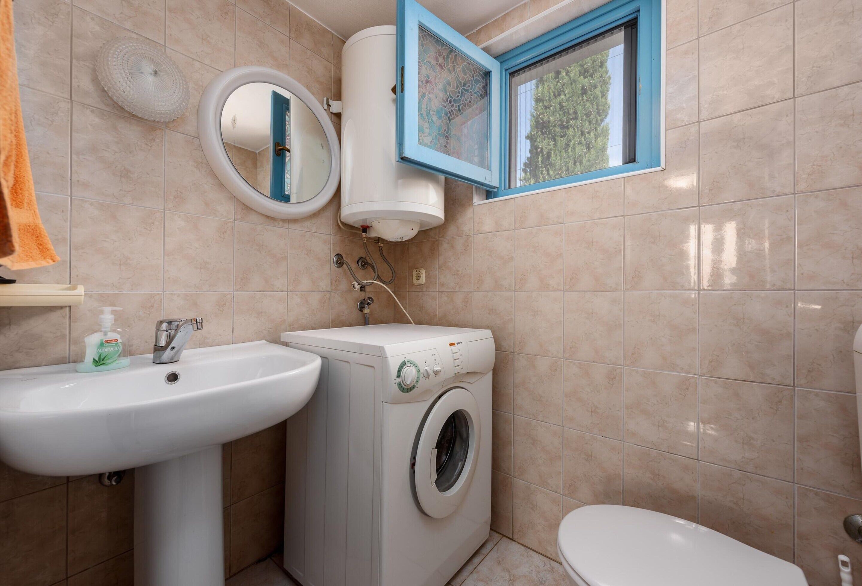 A bathroom with a sink, a washing machine, and a toilet.