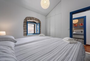 Quarto com cama, janela em arco de pedra, guarda-roupa e espelho com obras de arte.