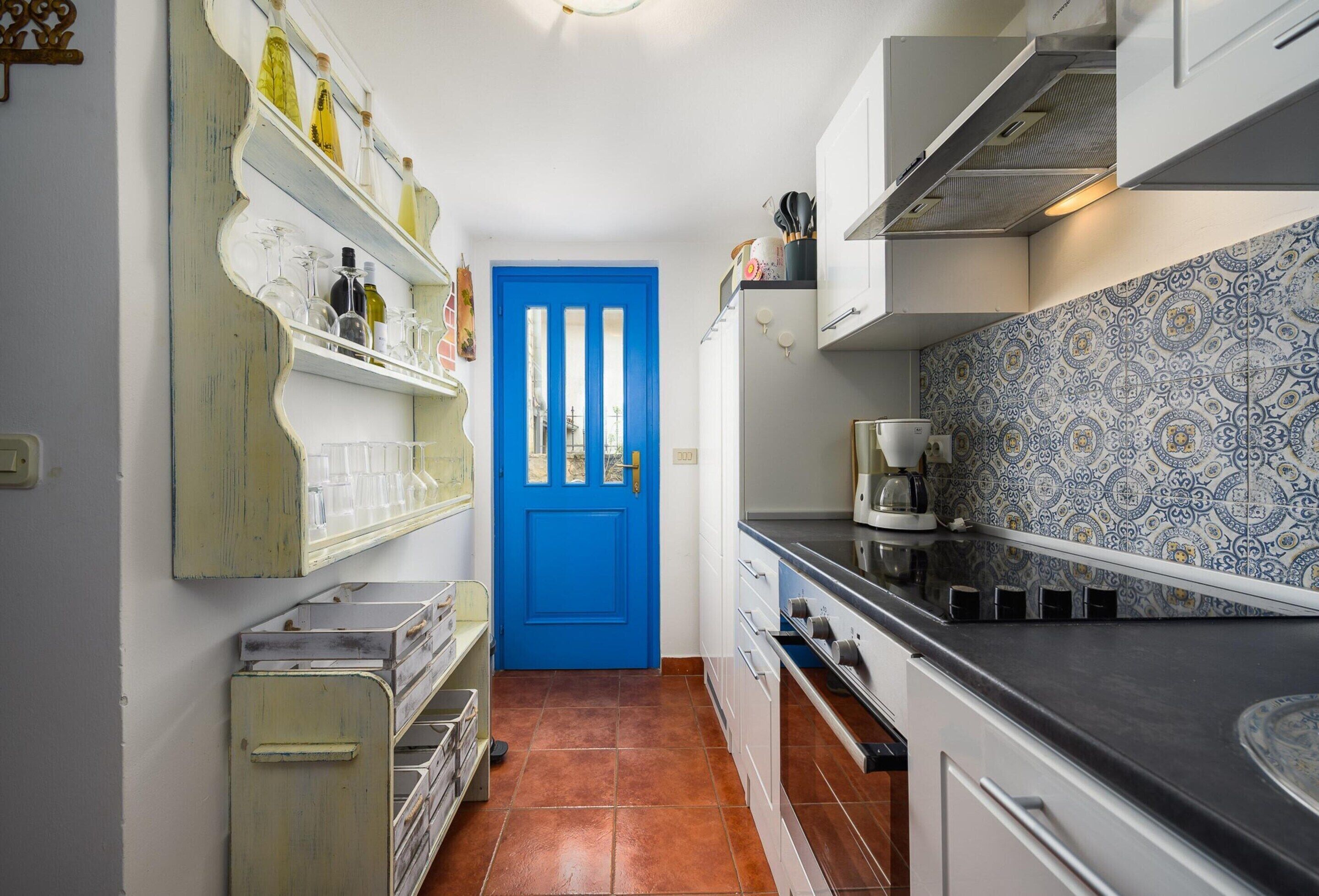 Una cocina estrecha con puerta azul, armarios blancos y salpicadero con diseño.