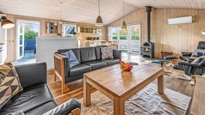 A spacious living area with a wooden ceiling, a black leather sofa, a wooden coffee table, and a fireplace. - "Efka" - 600m to the fjord by Interhome (Tarm)