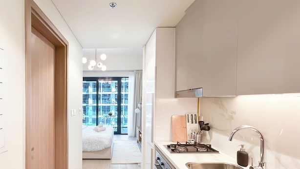 A modern kitchen with a stainless steel sink, a gas stove, and a countertop with kitchen utensils. - Urban Charm: Studio With Balcony in Riviera (Dubai)