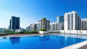 A rooftop swimming pool with a clear blue water surface, surrounded by modern high-rise buildings. - Urban Charm: Studio With Balcony in Riviera (Dubai)