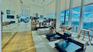 A spacious, modern interior with large windows, a central seating area, and a visible cityscape view.