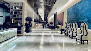 A spacious lobby with a marble reception desk, seating area, and a large abstract painting on the wall.