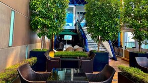 An outdoor seating area with wicker furniture and potted plants, a staircase, and a modern building facade. - The Platinum Suites KLCC By Sky Pool (Kuala Lumpur)