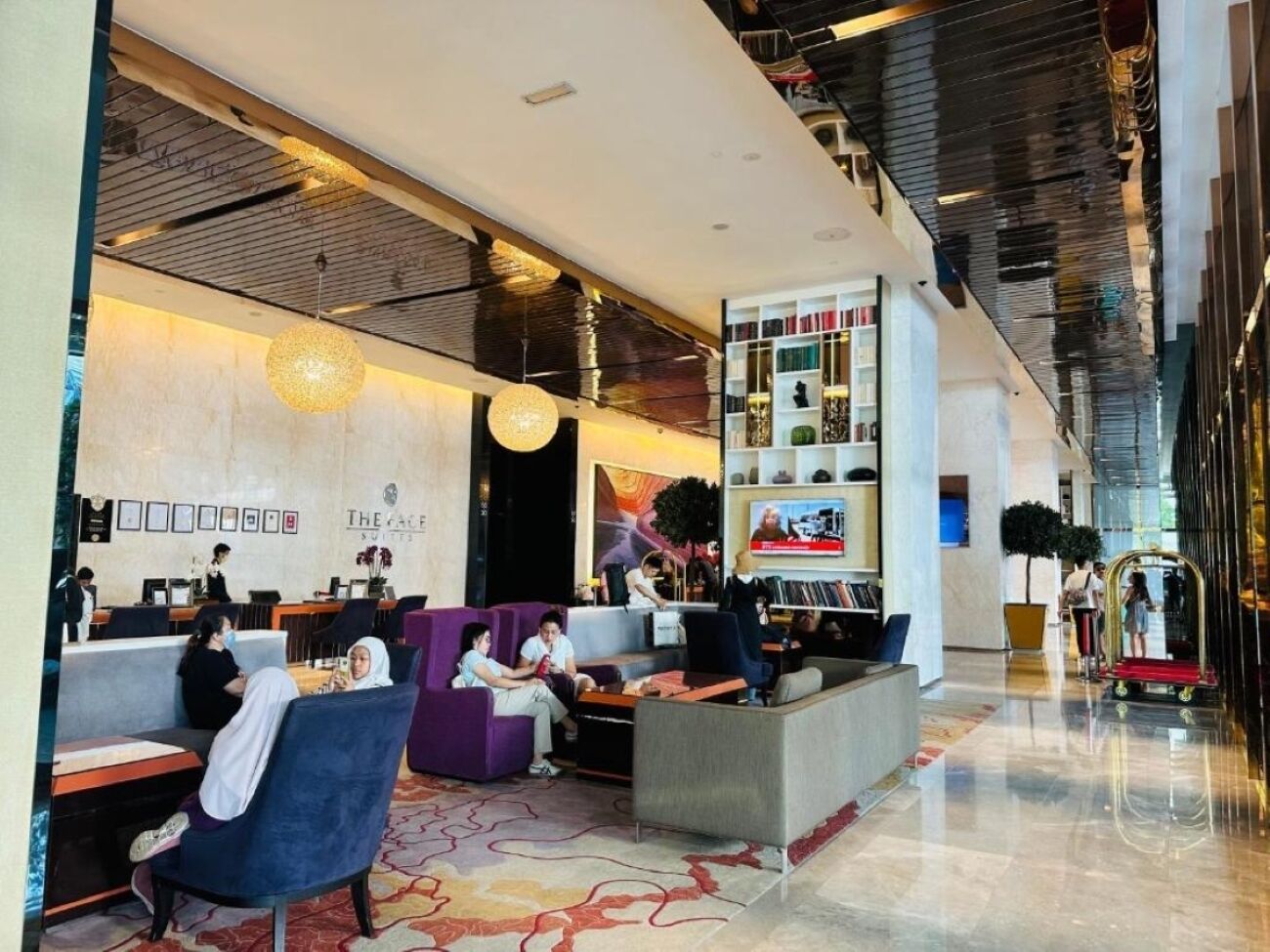 A modern hotel lobby with seating areas, a reception desk, and a television screen.