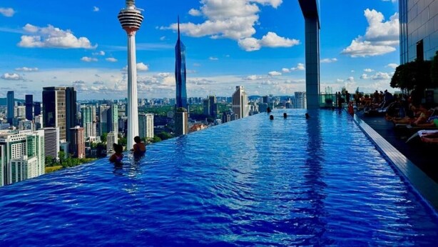A rooftop infinity pool with a cityscape view, including a prominent tower.