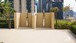 Une place urbaine moderne au design minimaliste, caractérisée par une structure murale de couleur beige, un petit espace paysager avec des plantes et une vue dégagée sur les gratte-ciel en arrière-plan.
