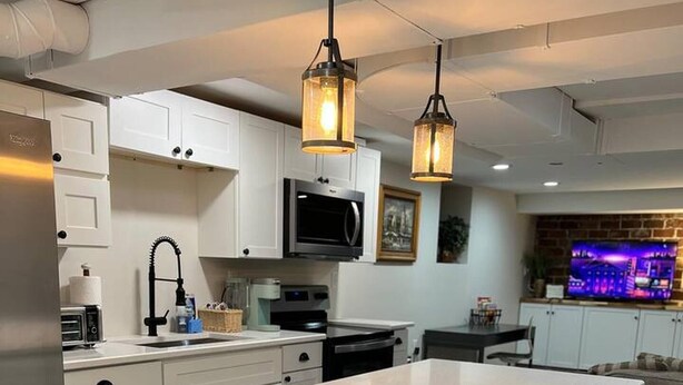 A modern kitchen with white cabinetry, a central island, pendant lighting, and a dining area with a sofa. - Private Garden Unit Gary BP (Gary)