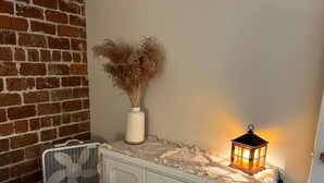 A white dresser with drawers, a white vase with dried plants, a white fan, and a lit lantern on a table. - Private Garden Unit Gary BP (Gary)