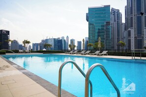 A swimming pool with lounge chairs and a cityscape in the background. - Exclusive Burj Crown 4b Balcony City Views (Dubai)