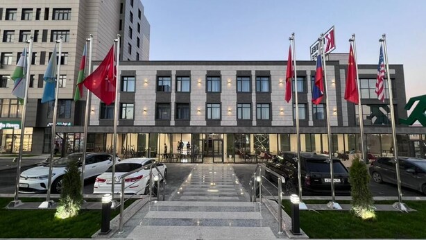 A modern building with a glass facade, multiple flags, and a parking lot with cars. - K HOTEL RESTURANT (Bishkek)