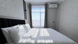 A hotel room with a large bed, a headboard, a window with curtains, and an air conditioning unit on the wall. - K HOTEL RESTURANT (Bishkek)