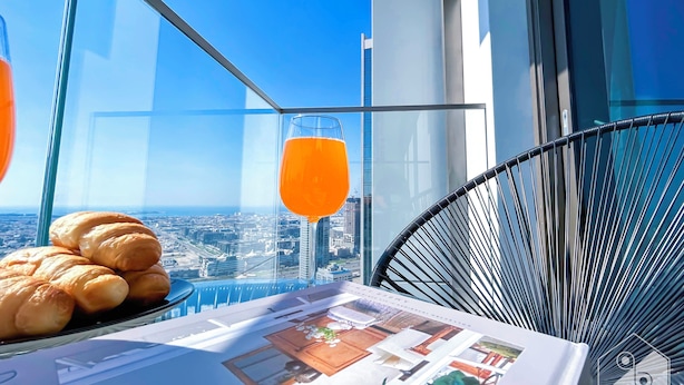 Een balkon met een glazen tafel, croissants, een glas sinaasappelsap en uitzicht over de stad.