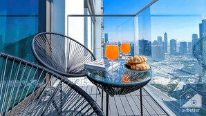 Een balkon met een glazen tafel, twee stoelen, twee glaasjes sinaasappelsap en een croissant.