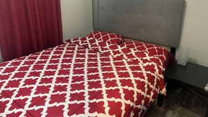 Un lit avec une tête de lit grise, une couvre-lit à motifs rouges et blancs, et une table de chevet sombre.