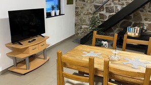 Uma área de refeições aconchegante com mesa e cadeiras de madeira, uma televisão sobre um móvel de madeira e uma parede de pedra.
