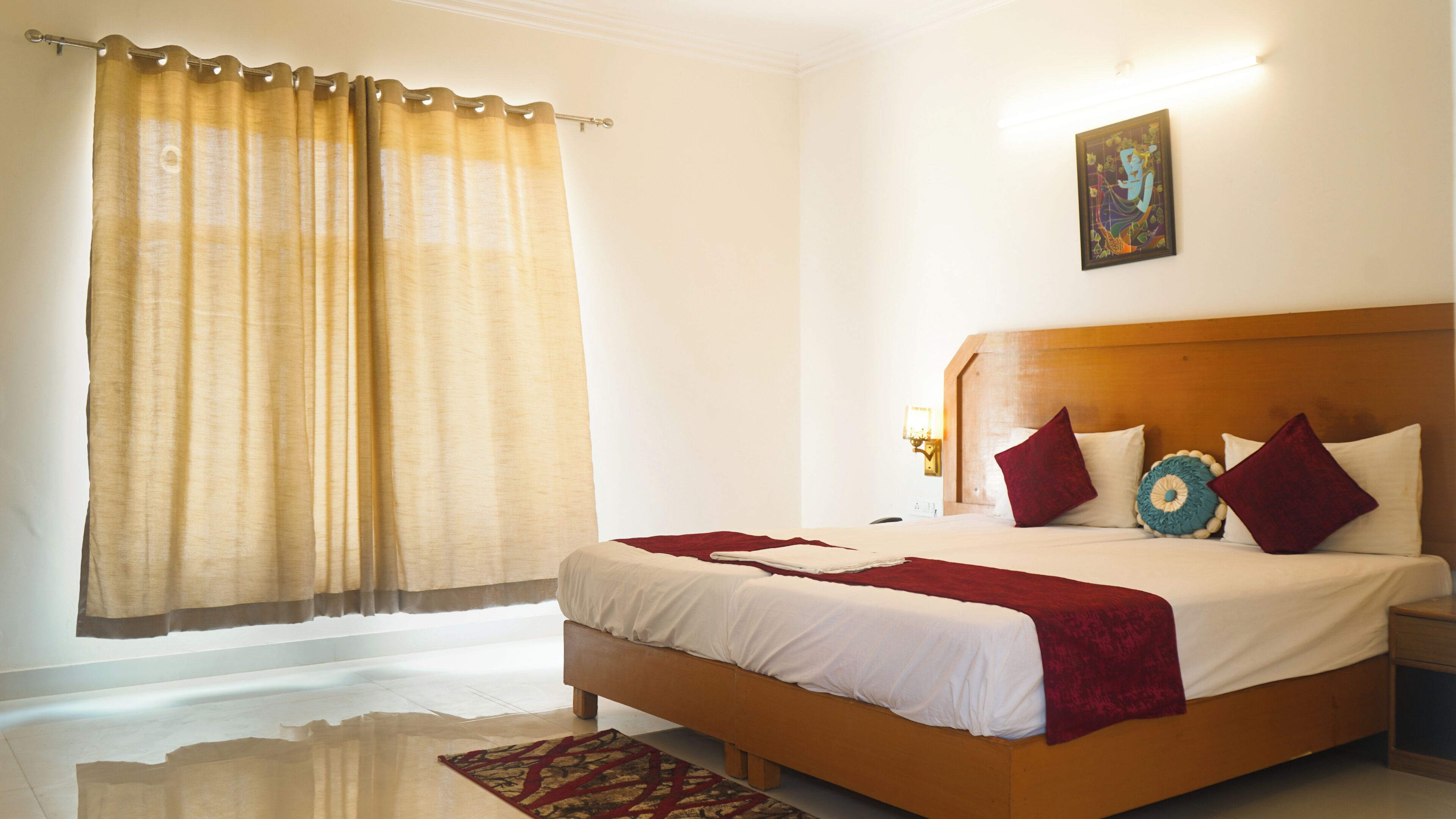 Une chambre d’hôtel avec un grand lit, une tête de lit en bois, un plaid rouge et un tableau accroché au mur.