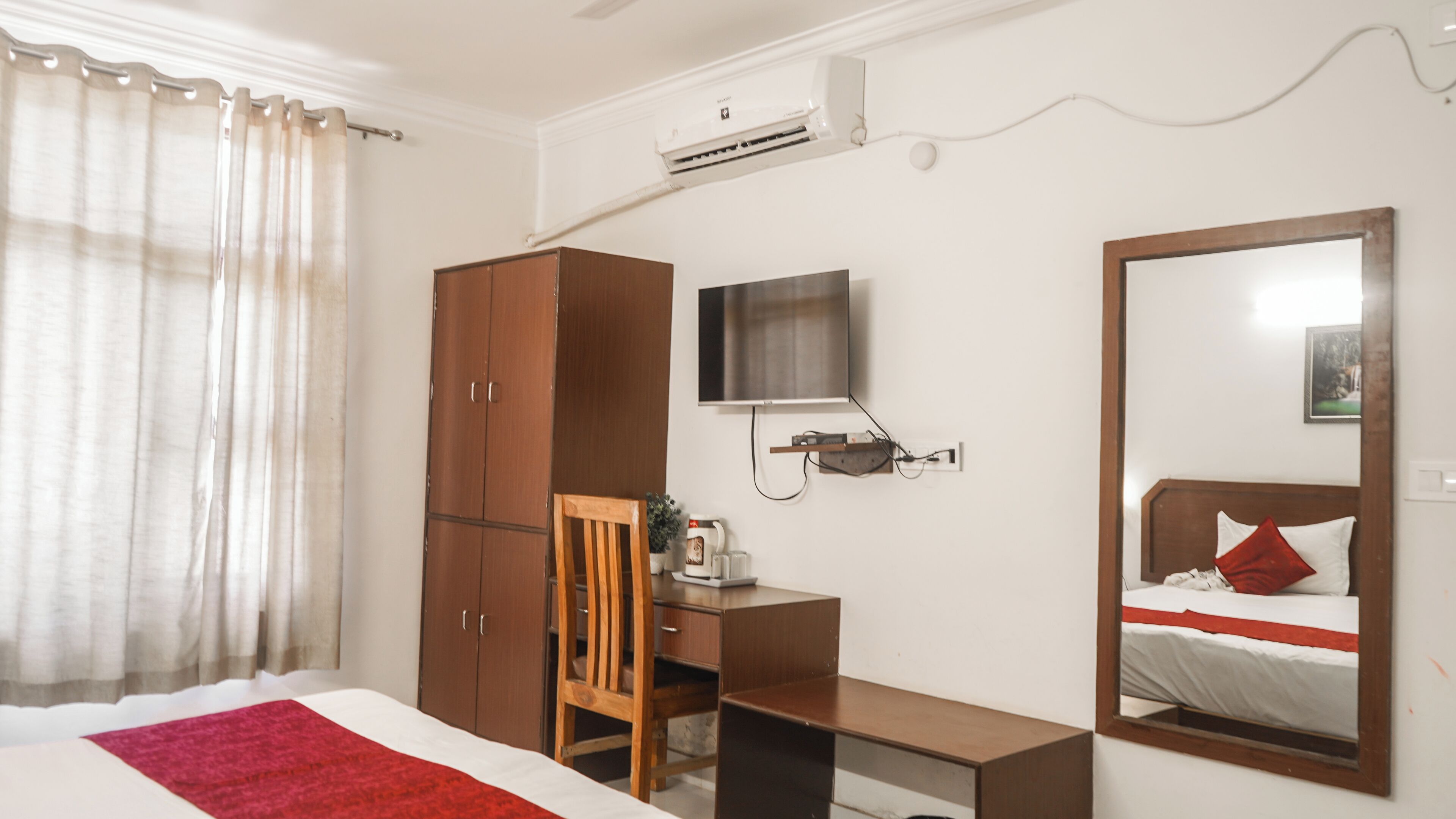 A hotel room with a bed, a desk, a wardrobe, a TV, and a mirror.