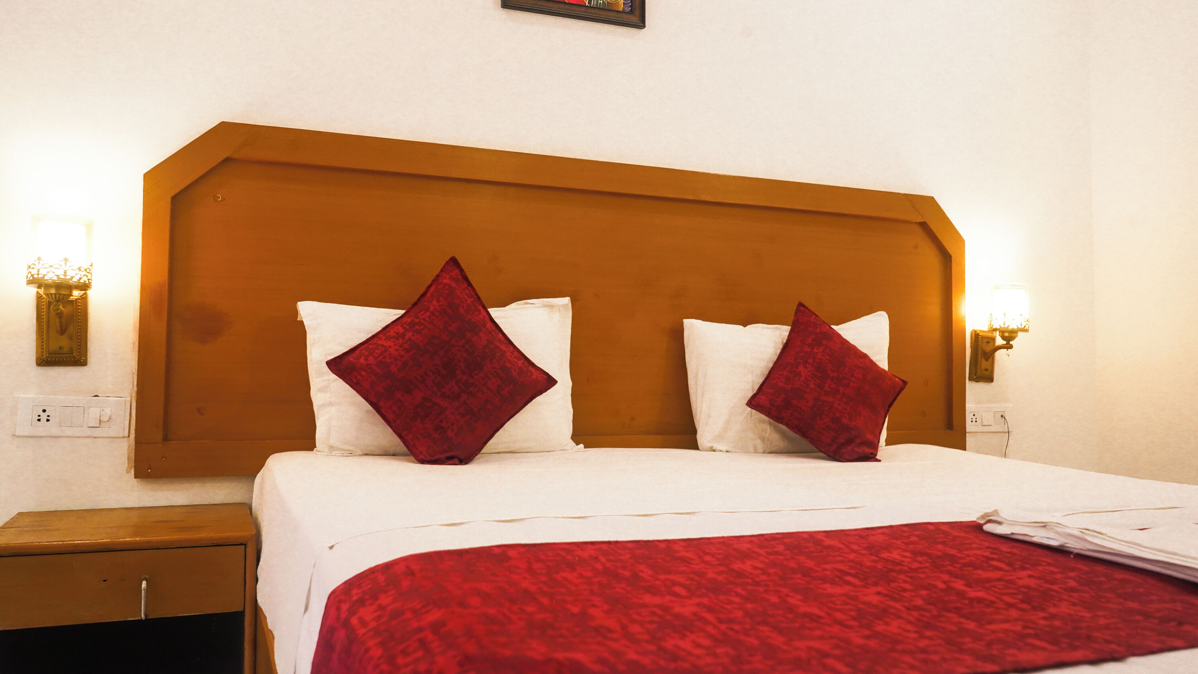 A hotel room with a wooden headboard, two white pillows, and a red throw blanket.