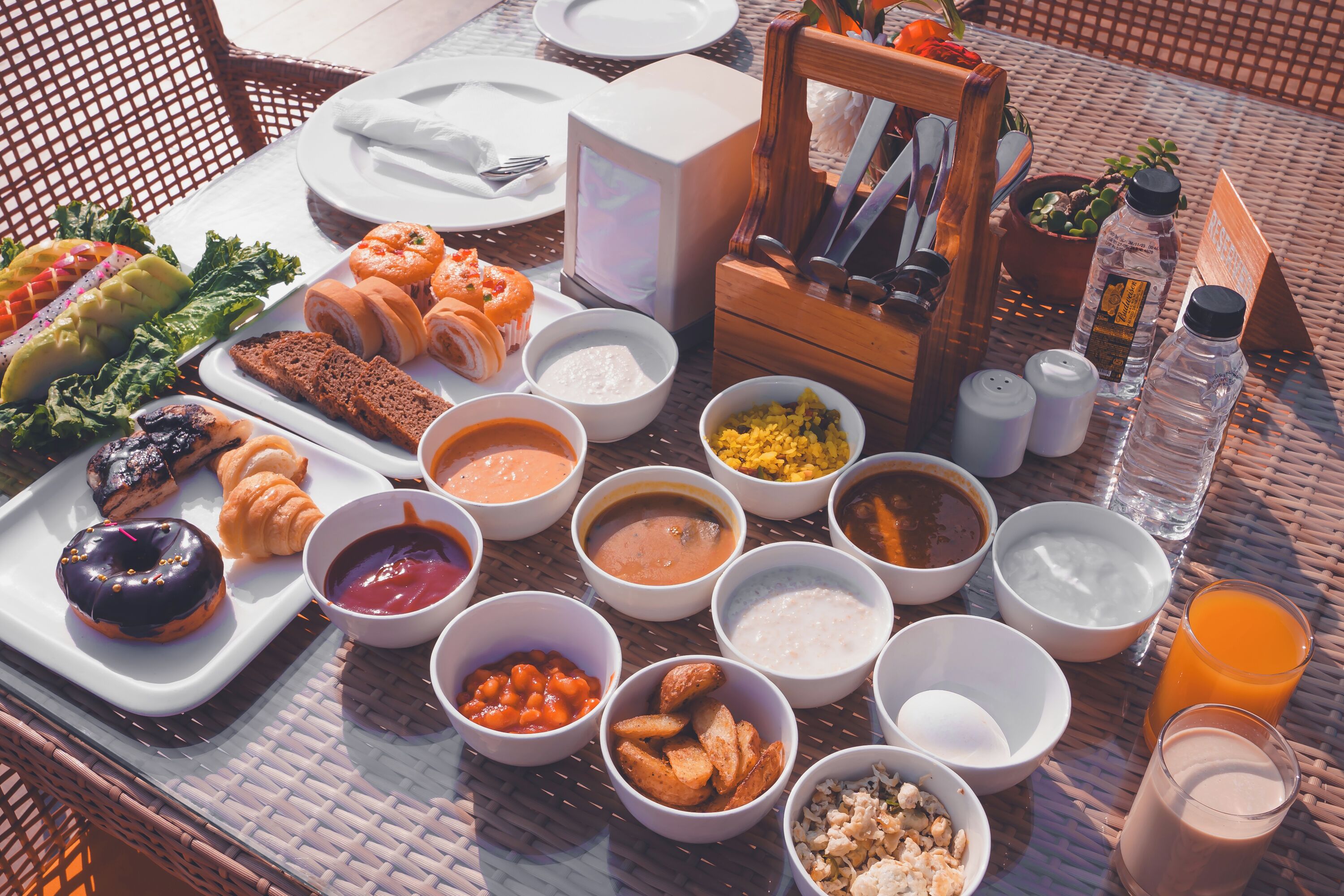 A breakfast spread on a wicker table with various dishes, including pastries, fruits, and beverages.