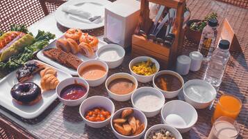 A breakfast spread on a wicker table with various dishes, including pastries, fruits, and beverages.