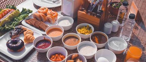 A breakfast spread on a wicker table with various dishes, including pastries, fruits, and beverages.