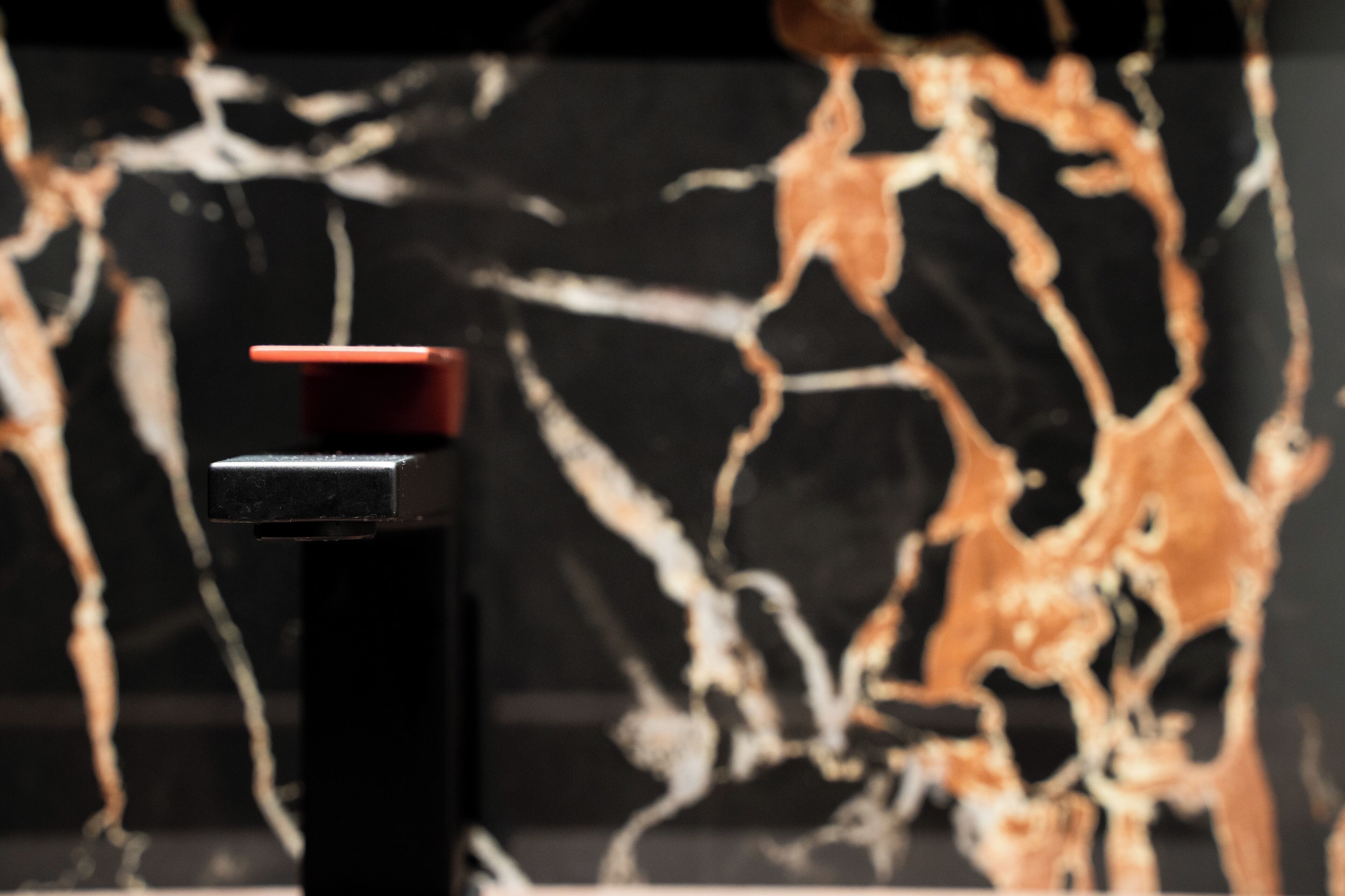 A close-up of a black object with a red top, possibly a bottle, against a background with a marbled pattern.