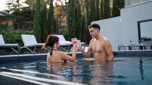 A couple in a swimming pool with lounge chairs and a modern building in the background. - Mon Luxury Rooms - Spa (Nicolosi)