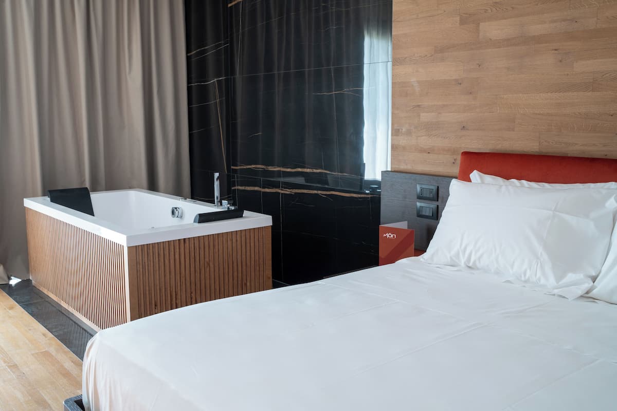 A modern hotel room with a large bed, a separate bathroom with a bathtub, and a wooden accent wall.