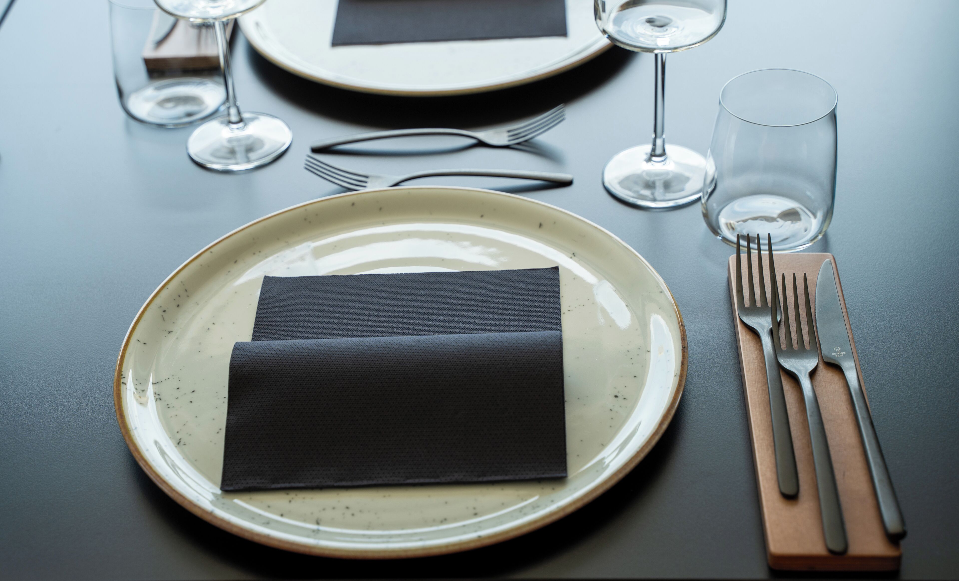 Una mesa servida con un plato, servilleta, cubiertos y copas de vino.