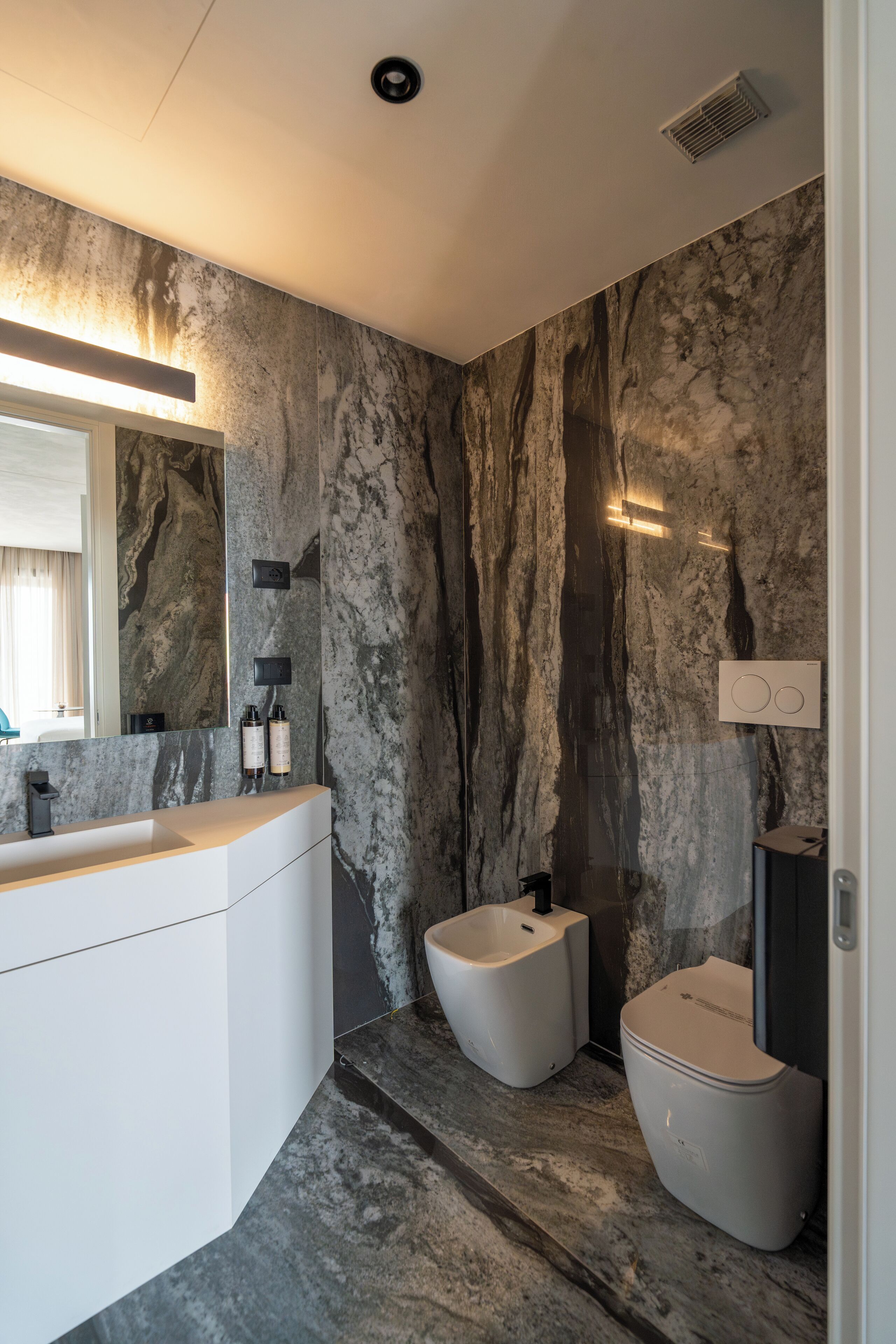 Une salle de bain moderne avec un mur en marbre, un lavabo blanc et des toilettes.
