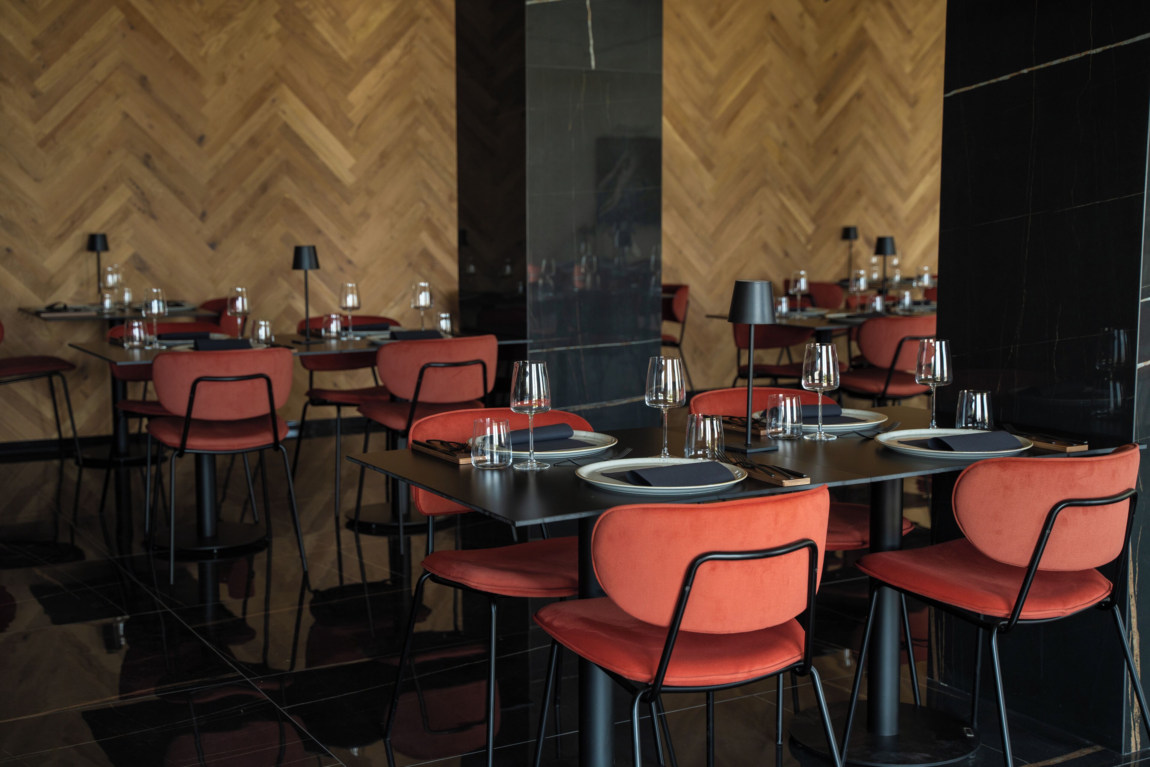 Un restaurant dont les tables sont dressées pour le service, avec des chaises rouges et une vaisselle noire.
