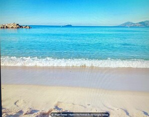 A beach with clear blue water, a sandy shore, and a rocky outcrop in the distance. - Vieux Port Studio for 4 with a Mezzanine Bedroom (Cannes)