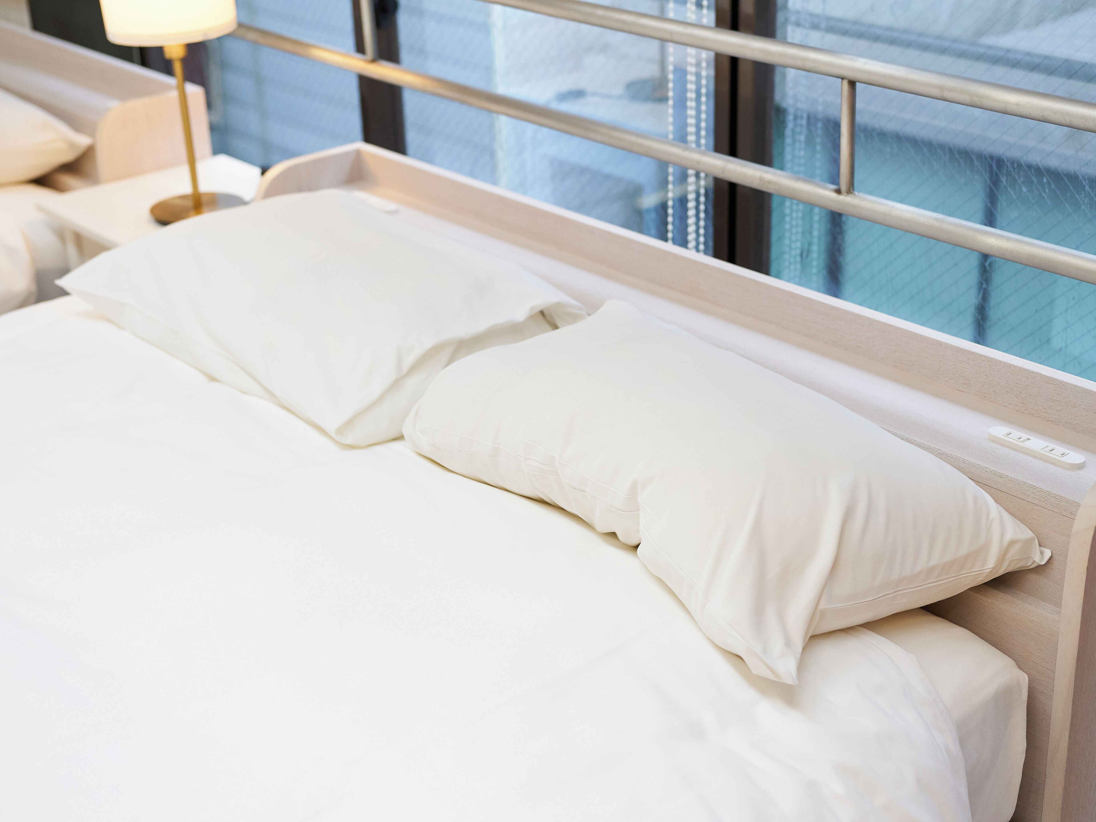 A hotel room with a bed, pillows, a bedside table, and a lamp.