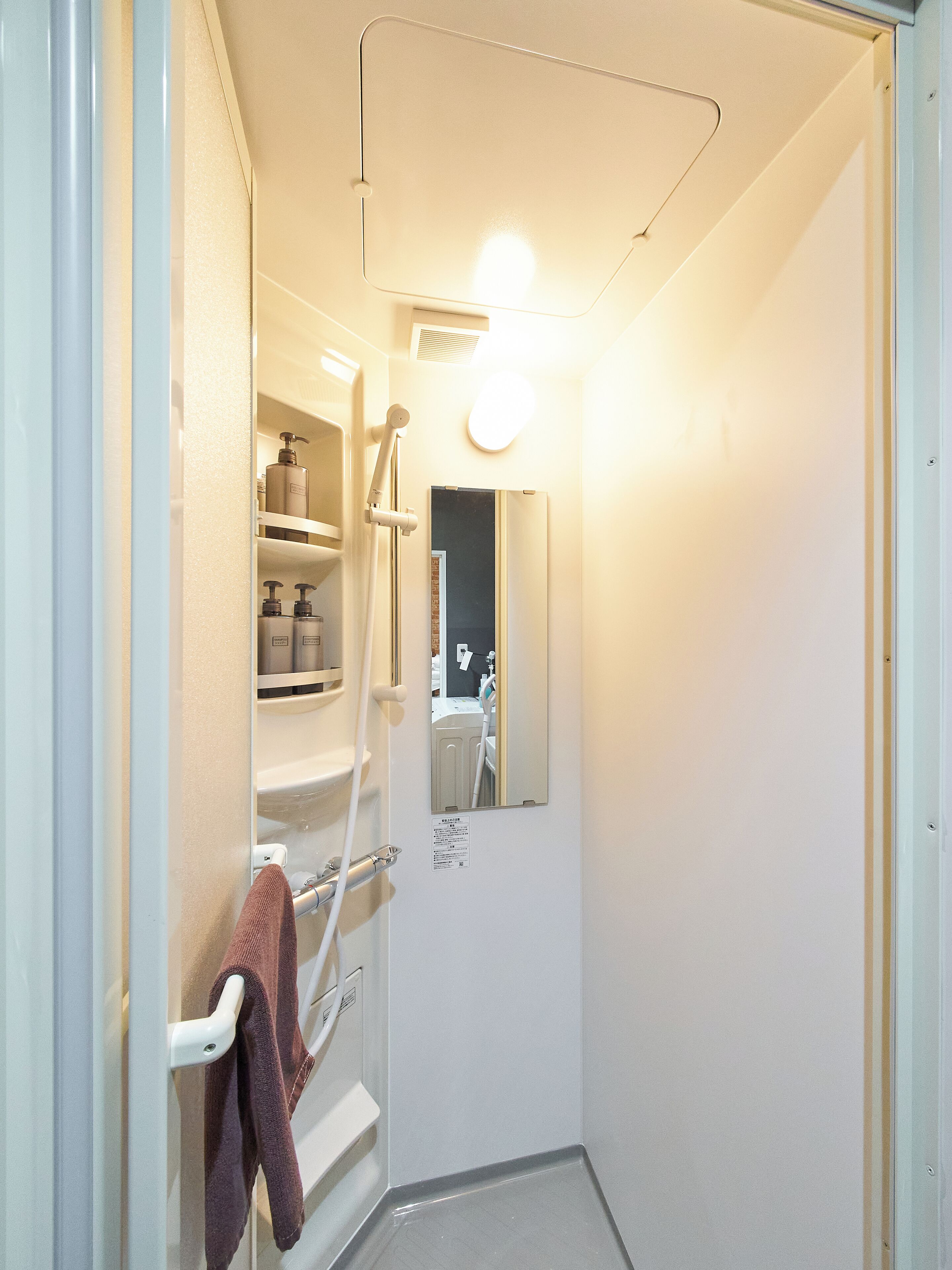 A narrow bathroom with a shower, a towel rack, and a mirror.