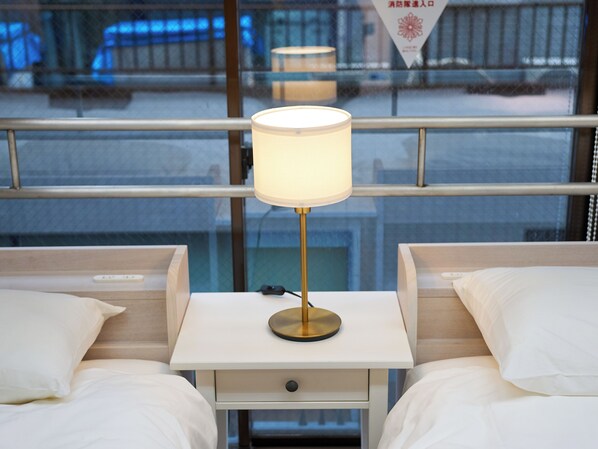 A hotel room with two beds, a bedside table with a lamp, and a window with a view of the outside.