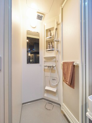 Een kleine, smalle badkamer met een douche, een handdoekhouder en een spiegel.