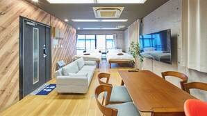Ein modernes Hotelzimmer mit Holzwand, einem großen Bett, einer Couch, einem Esstisch und einem an der Wand montierten Fernseher.